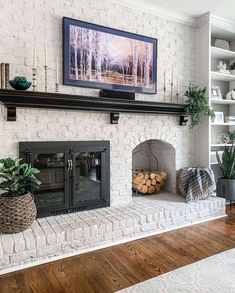 white brick wall fireplace recessed space for logs wood mantle candlesticks plants wall art 