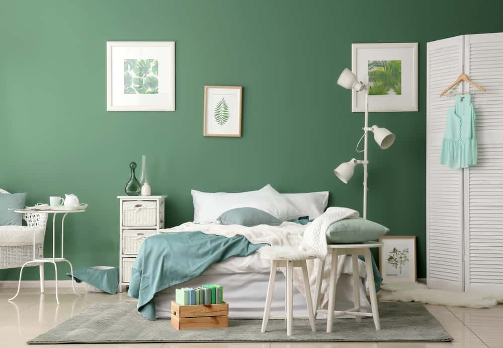 large green bedroom white bed table chair and shelving unit lamp framed leave paintings 