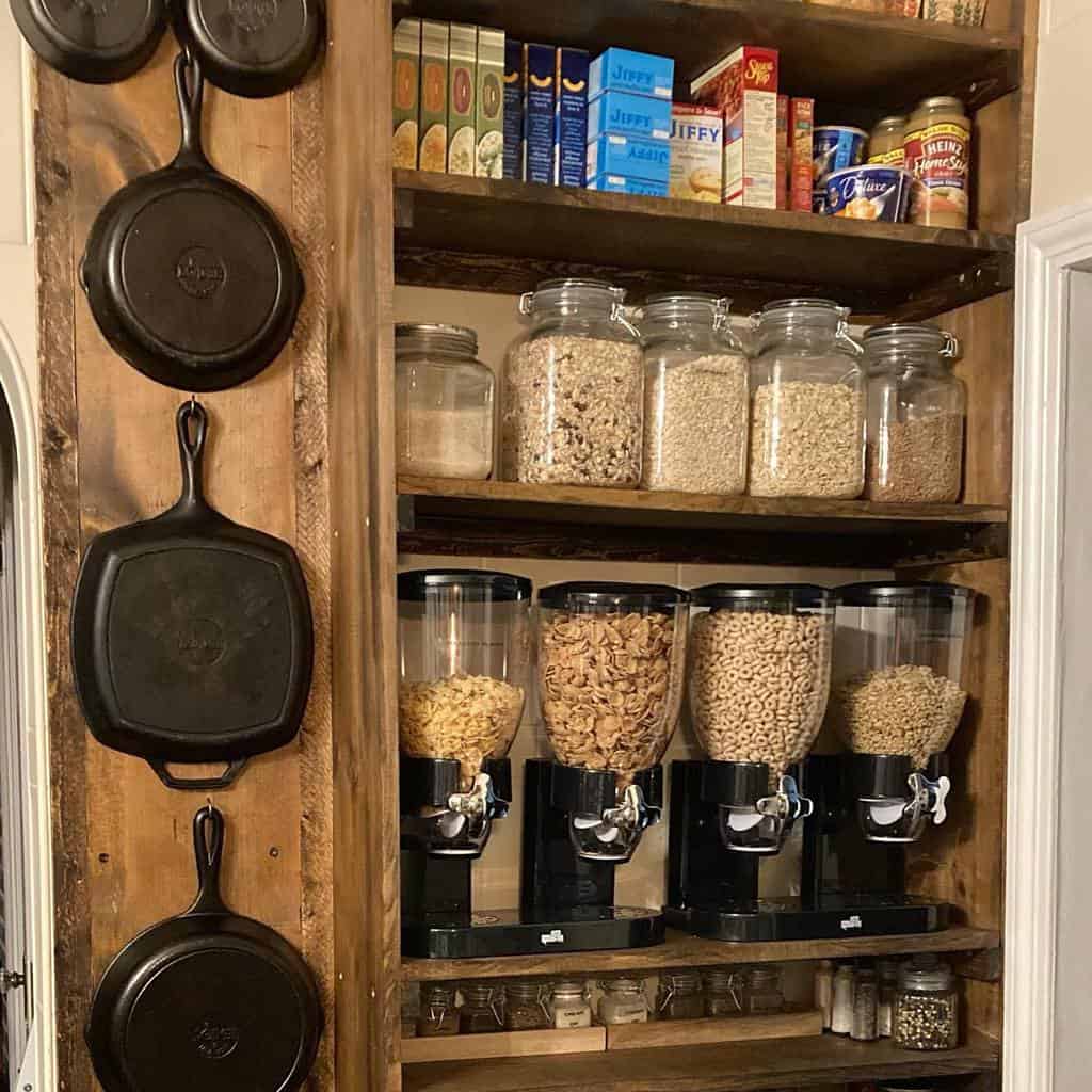 wood kitchen cabinet with breakfast cereal in jars and hanging pans 