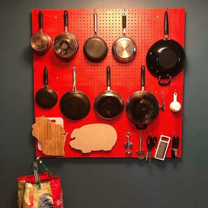 red pegboard in kitchen holding pots and pans 