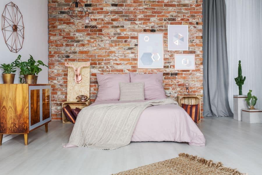 modern bedroom brick accent wall purple bedspread cactus plants wood crate bedside tables 